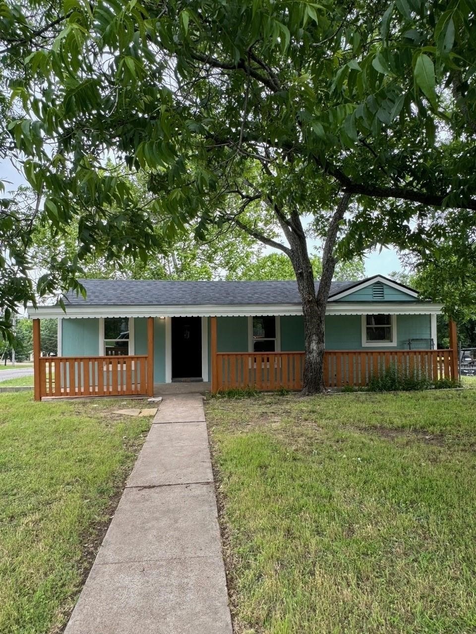 Ranch-style home featuring a front yard, covered porch, and a shingled roof