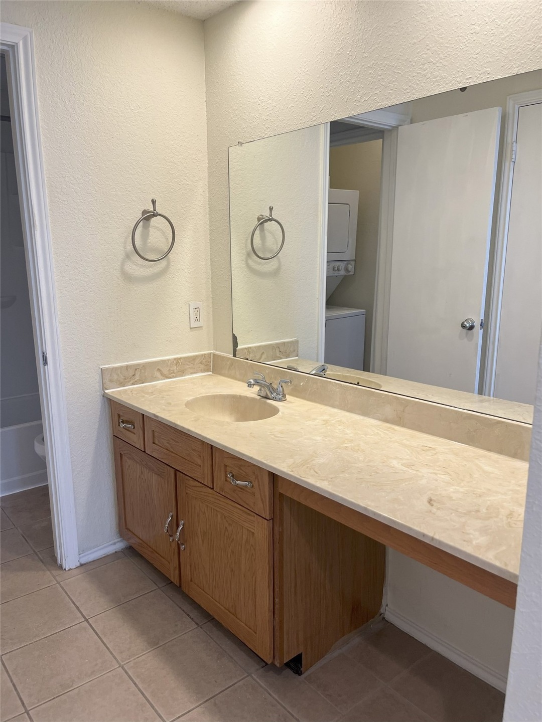 Bathroom featuring a textured wall, light tile patterned floors, vanity, and estacked washer and dryer