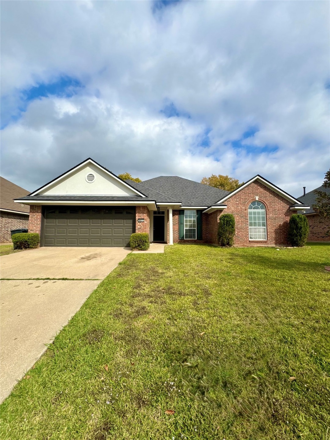 Single story home featuring concrete driveway, brick siding, a garage, a front lawn, and roof with shingles