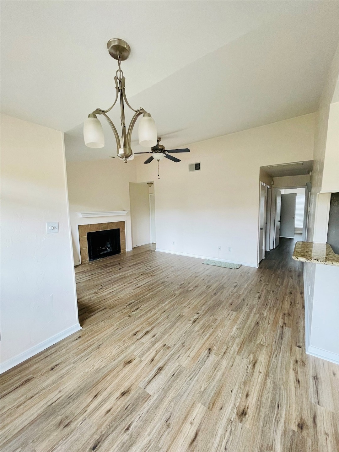 Unfurnished living room with a tiled fireplace, a ceiling fan, and light wood-style flooring