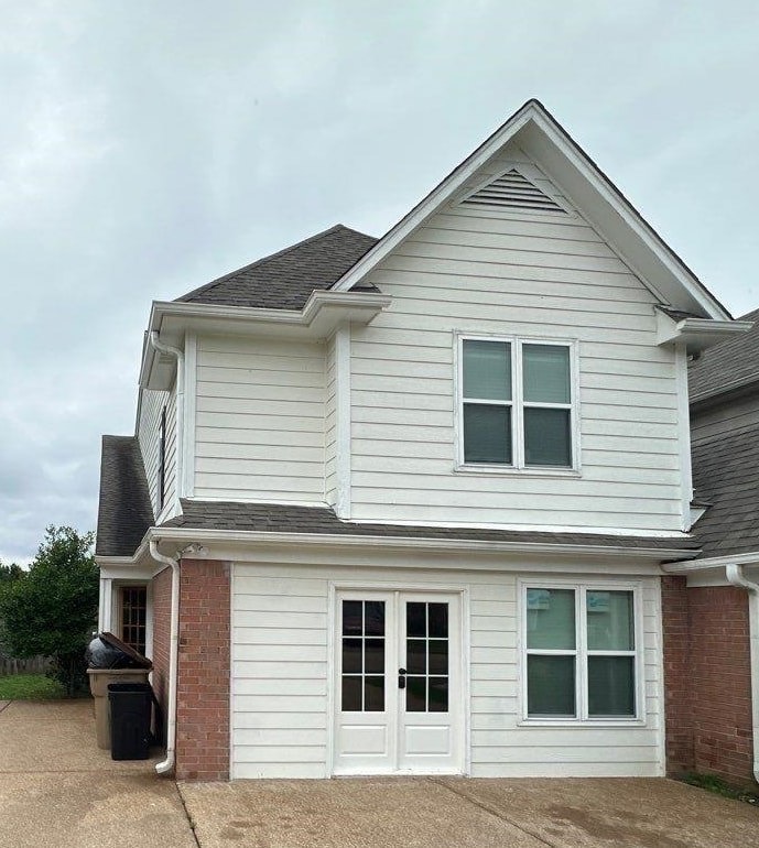 View of front facade with brick siding, french doors, and a shingled roof