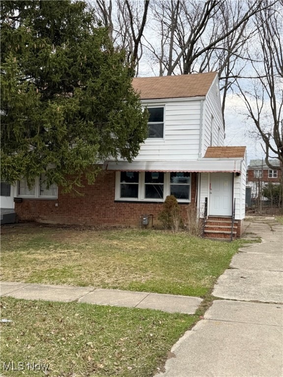 View of front facade with driveway, brick siding, a front lawn, a shingled roof, and entry steps