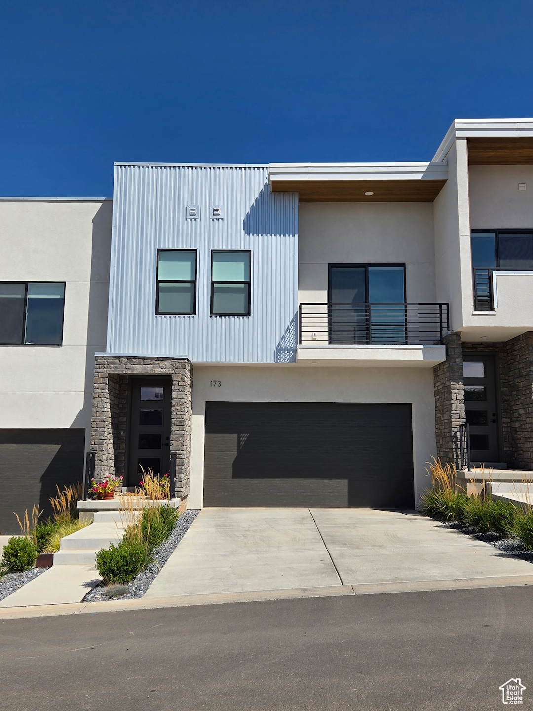 Contemporary home with stone siding, a balcony, driveway, stucco siding, and a garage