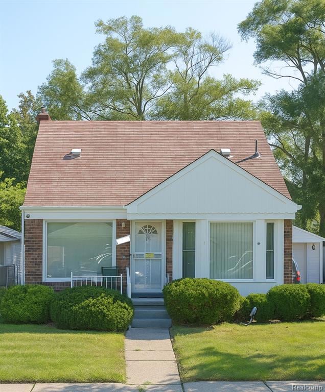 View of front of house with a front lawn, brick siding, roof with shingles, and a chimney