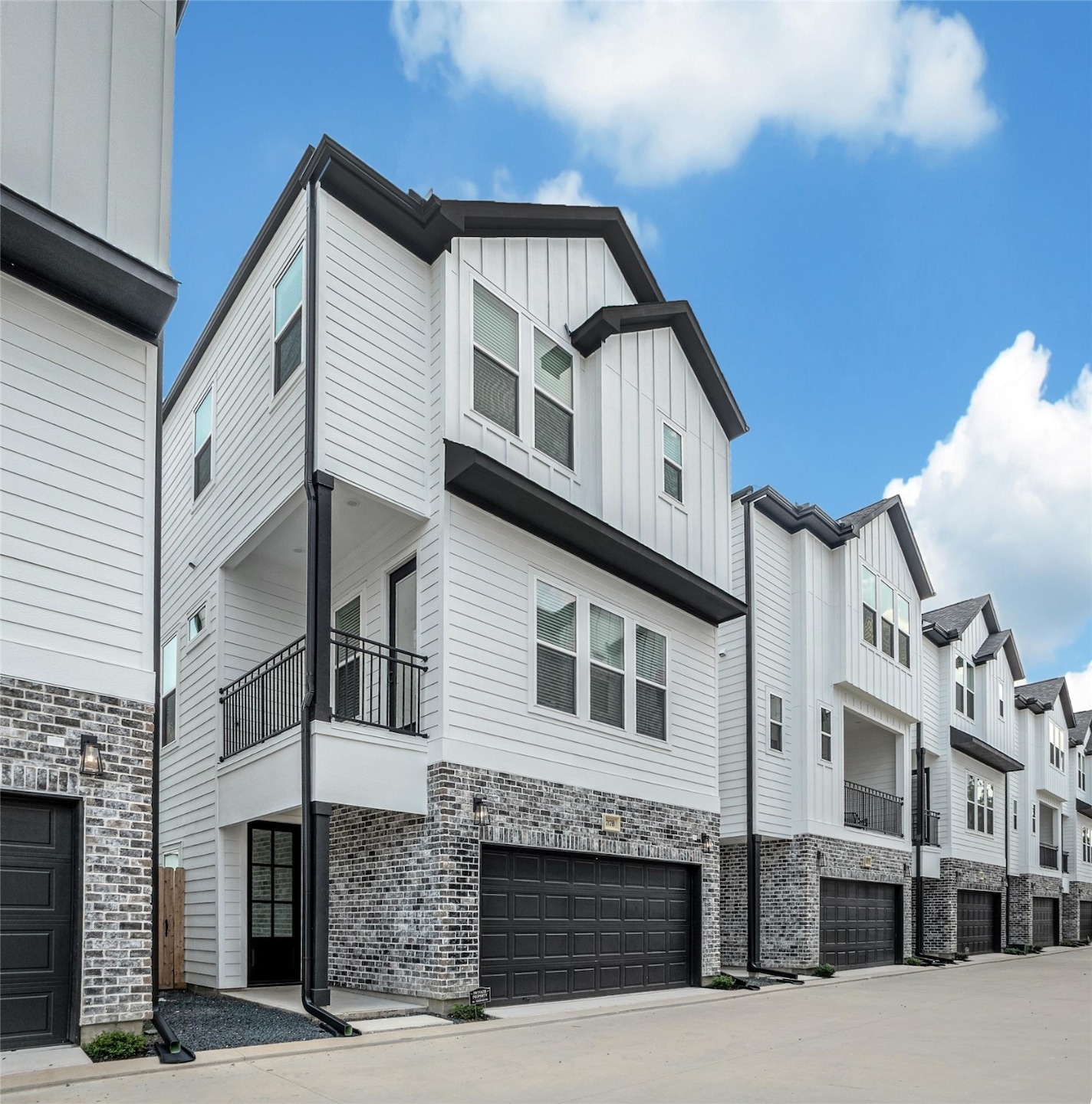 Modern townhouse with a clean, white exterior and black trim, featuring a brick lower facade. Each home balances farmhouse charm with urban convenience.