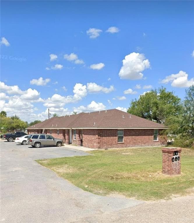 View of property exterior with uncovered parking, a yard, and brick siding