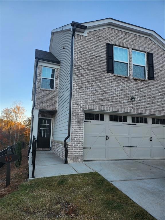 View of front of property featuring an attached garage, concrete driveway, and brick siding