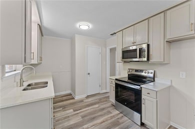 Kitchen featuring stainless steel appliances, light stone counters, light wood-style flooring, and ornamental molding