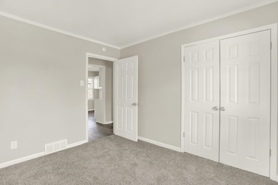 Unfurnished bedroom with dark carpet, ornamental molding, baseboards, and a closet