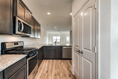 Kitchen with stainless steel appliances, dark brown cabinets, light wood finished floors, recessed lighting, and light stone counters