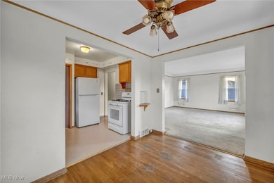 Kitchen with white appliances, crown molding, brown cabinetry, light wood-style flooring, and a ceiling fan