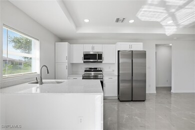 Kitchen featuring light stone counters, appliances with stainless steel finishes, white cabinets, recessed lighting, and a raised ceiling