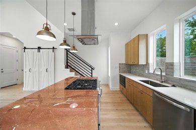 Kitchen featuring a barn door, light wood-style floors, appliances with stainless steel finishes, light stone counters, and recessed lighting