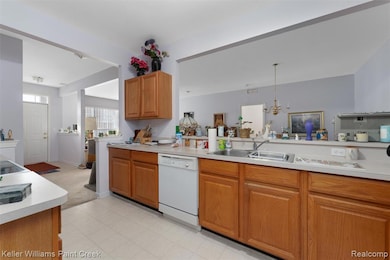 Kitchen with light countertops, dishwasher, brown cabinetry, and a chandelier