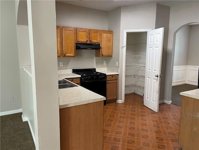 Kitchen featuring arched walkways, brown cabinetry, gas stove, light countertops, and under cabinet range hood