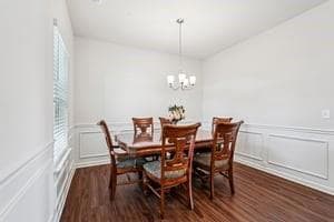 Dining room with a decorative wall, dark wood-style floors, a chandelier, and a wainscoted wall