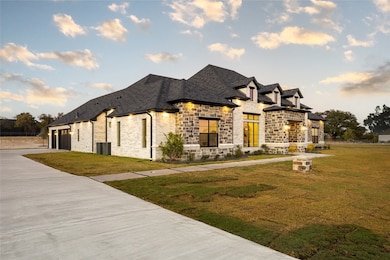 French country style house featuring a front lawn, stone siding, a garage, roof with shingles, and driveway
