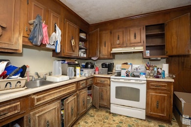 Kitchen featuring white electric stove, brown cabinets, under cabinet range hood, and open shelves