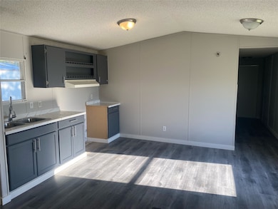 Kitchen with light countertops, a textured ceiling, dark wood-style flooring, open shelves, and lofted ceiling