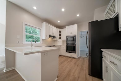Kitchen featuring appliances with stainless steel finishes, under cabinet range hood, a peninsula, a sink, and glass insert cabinets