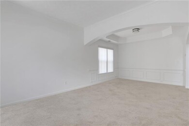 Carpeted empty room with arched walkways, ornamental molding, a decorative wall, a raised ceiling, and wainscoting