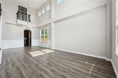 Living room featuring wood finished floors, stairway, a towering ceiling, a chandelier, and a decorative wall