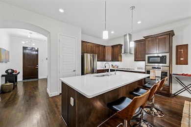 Kitchen featuring hanging light fixtures, appliances with stainless steel finishes, dark hardwood / wood-style floors, wall chimney exhaust hood, and sink