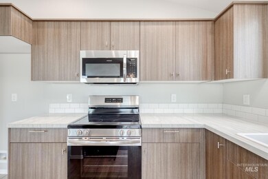 Kitchen with stainless steel appliances, light countertops, light brown cabinetry, vaulted ceiling, and modern cabinets