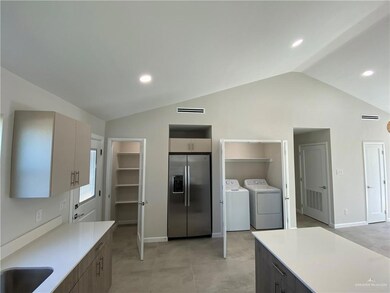 Kitchen with sink, light tile flooring, lofted ceiling, stainless steel fridge with ice dispenser, and independent washer and dryer