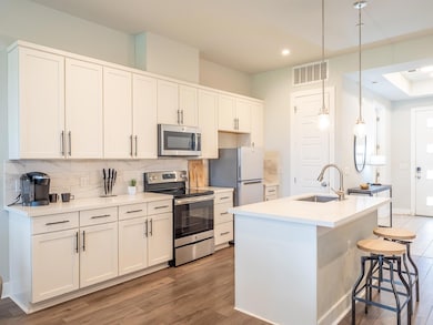 Kitchen with stainless steel appliances, decorative backsplash, pendant lighting, an island with sink, and white cabinetry