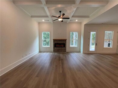 Unfurnished living room featuring coffered ceiling, dark wood-type flooring, a brick fireplace, beamed ceiling, and a ceiling fan
