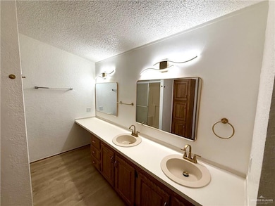 Bathroom featuring a textured ceiling, wood finished floors, double vanity, and a textured wall