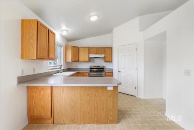 Kitchen with stainless steel electric range oven, lofted ceiling, light countertops, under cabinet range hood, and a peninsula