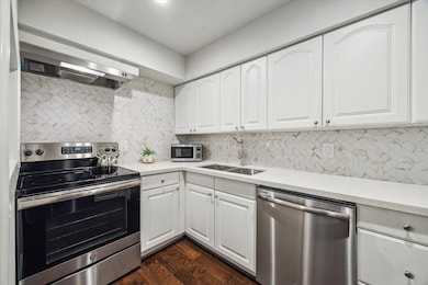 Alternate view of the kitchen showcasing the marble-like counter to ceiling backsplash, along with a GE Dishwasher and GE stainless electric range and venthood above. Microwave remains.