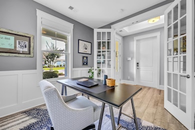 Office area featuring light wood finished floors, a wainscoted wall, french doors, and a decorative wall
