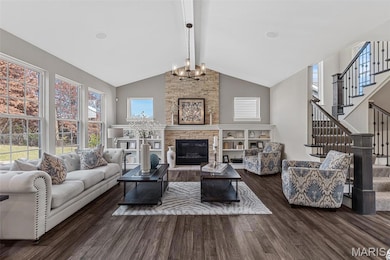 Living area featuring beamed ceiling, stairway, a stone fireplace, dark wood finished floors, and a chandelier