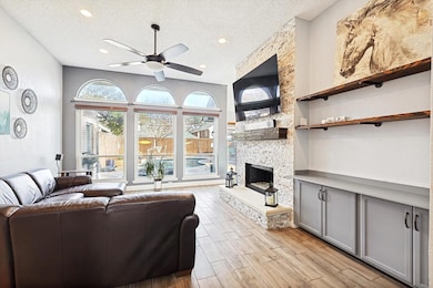 Living room featuring ceiling fan, a stone fireplace, a textured ceiling, and light wood-type flooring