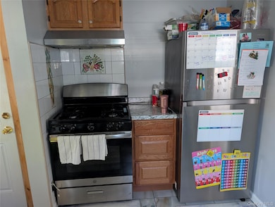Kitchen with brown cabinets, appliances with stainless steel finishes, light countertops, and exhaust hood