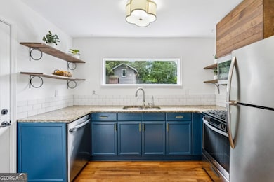A stunning modern kitchen pairs dark blue cabinetry with gold hardware, a crisp white tile backsplash and open shelving. The kitchen boasts plenty of granite countertop space and includes a full stainless appliance package.