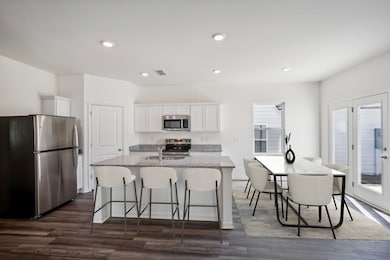 Kitchen featuring appliances with stainless steel finishes, white cabinets, light stone counters, a breakfast bar, and an island with sink