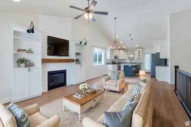 Living area with high vaulted ceiling, light wood-style floors, ceiling fan, a fireplace, and baseboards