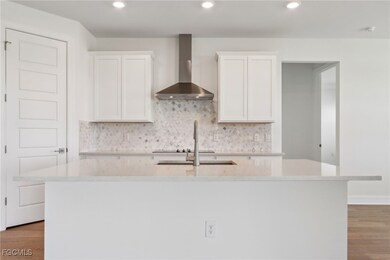 Kitchen featuring light wood-style floors, white cabinetry, wall chimney exhaust hood, light stone countertops, and recessed lighting