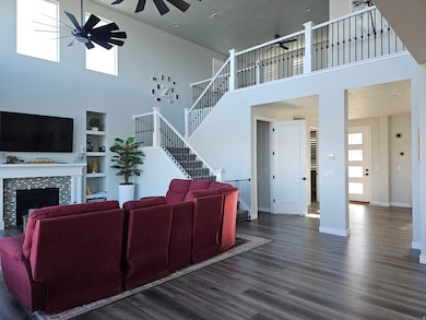 Living area with a high ceiling, LVP floors, a tile fireplace, stairway, and ceiling fan