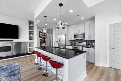 Kitchen with appliances with stainless steel finishes, light wood finished floors, dark countertops, a sink, and a breakfast bar