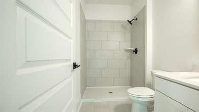 Bathroom with toilet, vanity, tiled shower, and tile patterned flooring
