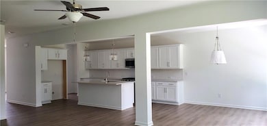 Kitchen featuring wood finished floors, stainless steel microwave, a ceiling fan, white cabinetry, and a sink