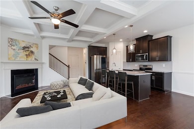 Living room with stairs, dark wood-style floors, beamed ceiling, a ceiling fan, and coffered ceiling