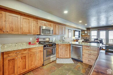 Kitchen featuring appliances with stainless steel finishes, a peninsula, light stone counters, open floor plan, and dark stone finish flooring