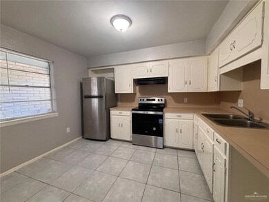 Kitchen with white cabinetry, under cabinet range hood, light tile patterned flooring, a sink, and stainless steel appliances