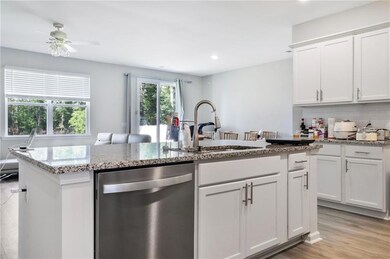 Kitchen with stainless steel dishwasher, a sink, white cabinetry, light stone countertops, and recessed lighting